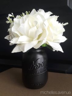 a black mason jar with white flowers in it