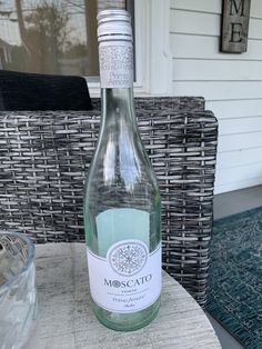 a bottle of wine sitting on top of a table next to a glass vase and wicker chair