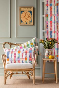 a chair and table with flowers in front of a colorful quilted wall hanging on the wall