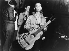 black and white photo of man holding guitar in front of other men standing around him