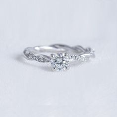 a white gold engagement ring with two diamonds on the band and a twisted vine design