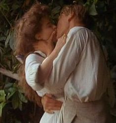 a man and woman kissing in front of trees