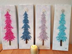 three christmas trees with glitter on them sitting next to a candle