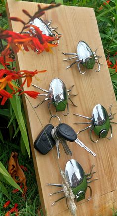 several metal bugs sitting on top of a wooden board next to red and orange flowers