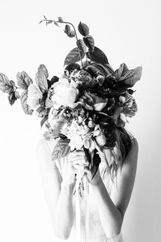 black and white photograph of a woman holding flowers in front of her face with both hands