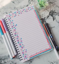 an open notepad next to two pens on a marble surface