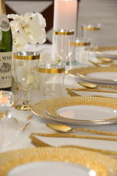 the table is set with white and gold plates, silverware, champagne bottles and candles