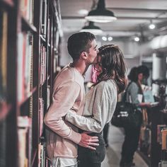 a man and woman kissing in front of bookshelves with people standing behind them