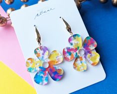 two colorful flower shaped earrings sitting on top of a white card next to some beads