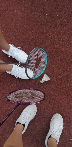 two people standing next to each other with tennis rackets and shoes on the ground