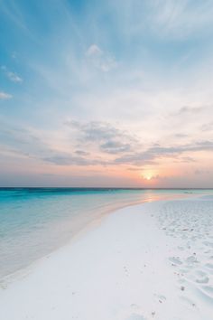 the sun is setting on an empty beach with footprints in the sand and water below