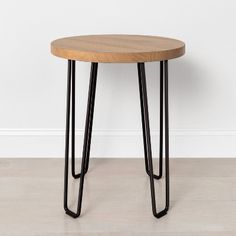 a round wooden table with metal legs on the floor next to a white wall in an empty room