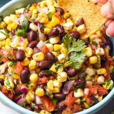 a hand dipping a tortilla chip into a bowl filled with corn and black beans