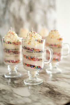 three glasses filled with white frosting and sprinkles on a marble counter