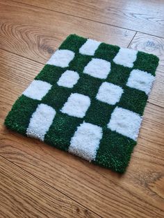 a green and white rug with squares on it sitting on top of a wooden floor