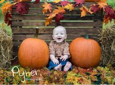 a baby sitting on hay with two pumpkins in front of it and fall leaves around him