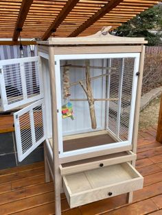 a bird cage sitting on top of a wooden floor next to a tree branch and window