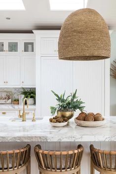 a kitchen with white cabinets and marble counter tops, two chairs at the center island