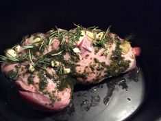 two pieces of meat covered in herbs and seasoning on top of a black plate