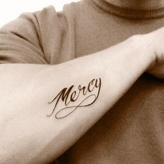 a man with a tattoo on his arm that says mercy in cursive writing