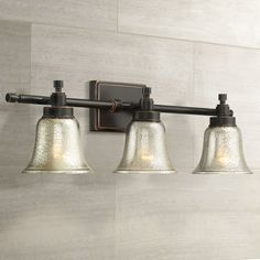 three light bathroom fixture with glass bell shades on the side and metal arm, in an old - fashioned finish