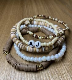 three different bracelets with beads and letters on them sitting on top of a wooden table