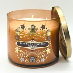 a candle with cinnamon sugared pecans in it on a white table next to a gold lid