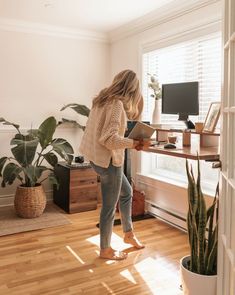 a woman standing in front of a computer on top of a wooden desk next to a potted plant