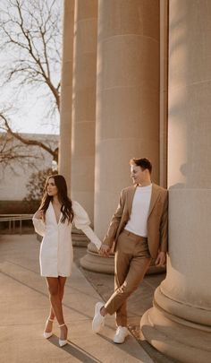 a man and woman holding hands while standing next to columns