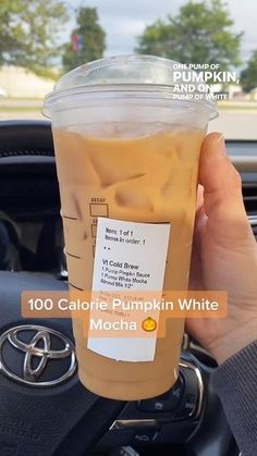 a person holding up a cup of iced coffee in their hand with the words, 100 calorie pumpkin white mocha on it