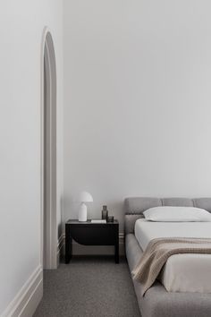 a bed sitting next to a white wall in a bedroom