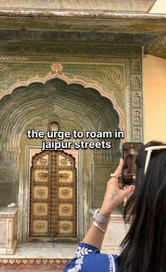 a woman taking a photo with her cell phone in front of an ornate doorway that reads, the urge to roam in jalpur streets