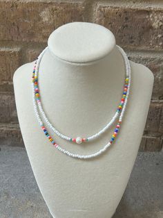 a white beaded necklace with multi colored beads on a mannequin neckline