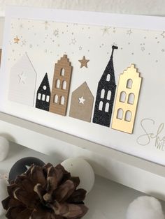 a christmas card with three houses and a pine cone on the table next to it