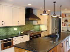 a kitchen with white cabinets, black counter tops and green tile backsplashes