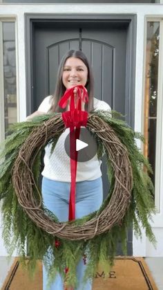 a woman standing in front of a door with a wreath on it and a red ribbon around her neck