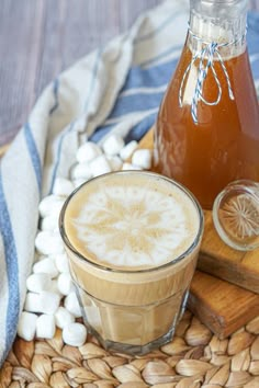 two glasses of iced coffee sit on a table next to a bottle of liquid and marshmallows