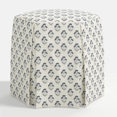 a white and blue patterned ottoman cover with an intricate design on the top, in front of