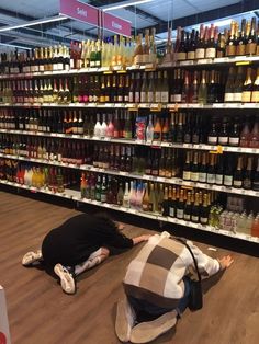 two people laying on the floor in front of shelves full of wine and liquor bottles