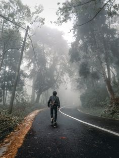 a person riding a skateboard down a road in the foggy forest on a cloudy day