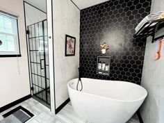 a white bath tub sitting next to a black and white tiled wall in a bathroom