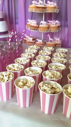 pink and white striped paper cups filled with popcorn on top of a table next to cupcakes