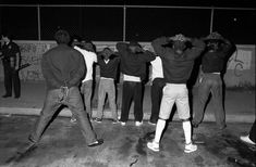 black and white photograph of people standing in front of a fence with their hands on their head