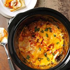 a crock pot filled with cheese and vegetables next to a plate of food on a table