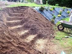 a man standing next to a pile of dirt near a wheelbarrow and fence