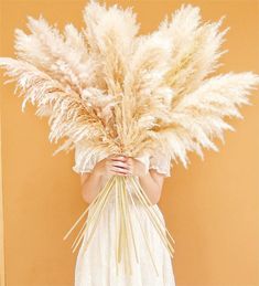 a woman holding a bunch of dry grass in front of her face and wearing a white dress