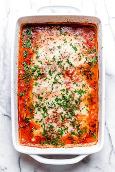 a casserole dish filled with meat, cheese and parsley on top of a marble counter