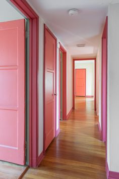 an empty hallway with pink doors and wood flooring on either side of the room