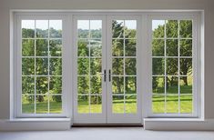 an empty room with double doors and windows overlooking the green grass field in the distance