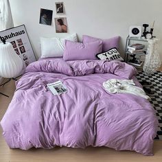 a bed with purple comforter and pillows in a room next to pictures on the wall